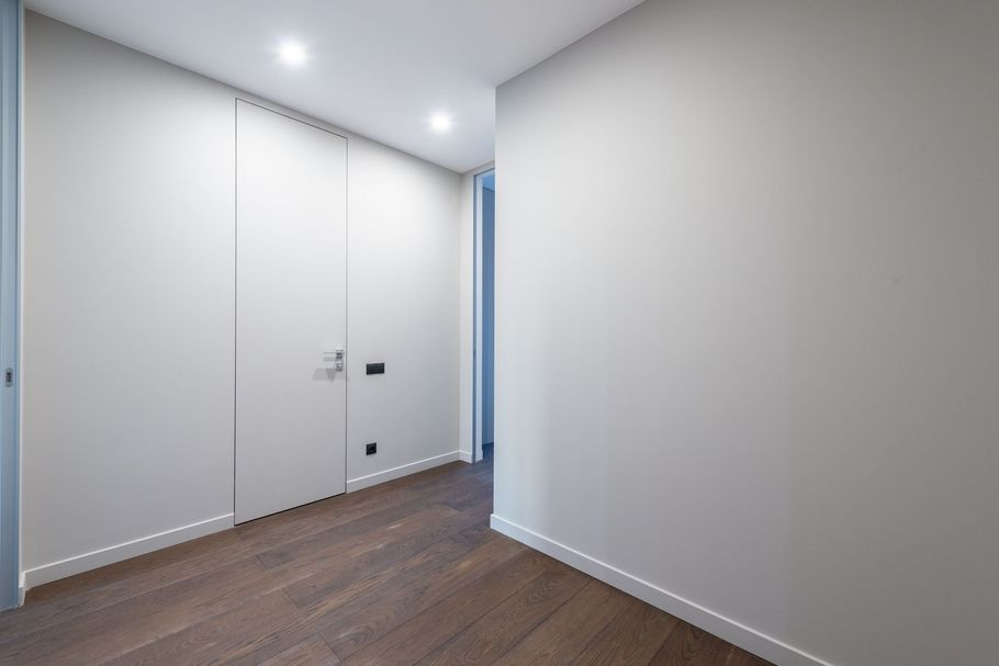 Empty white hallway with closed double doors, gray walls, and wood flooring.