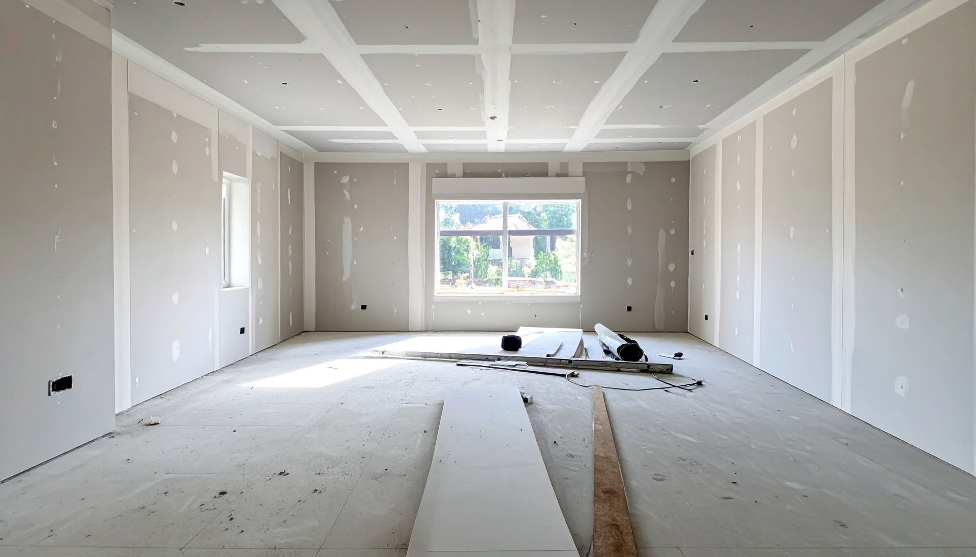 Empty unfinished room with drywall, debris on the floor, and a window at the far end.