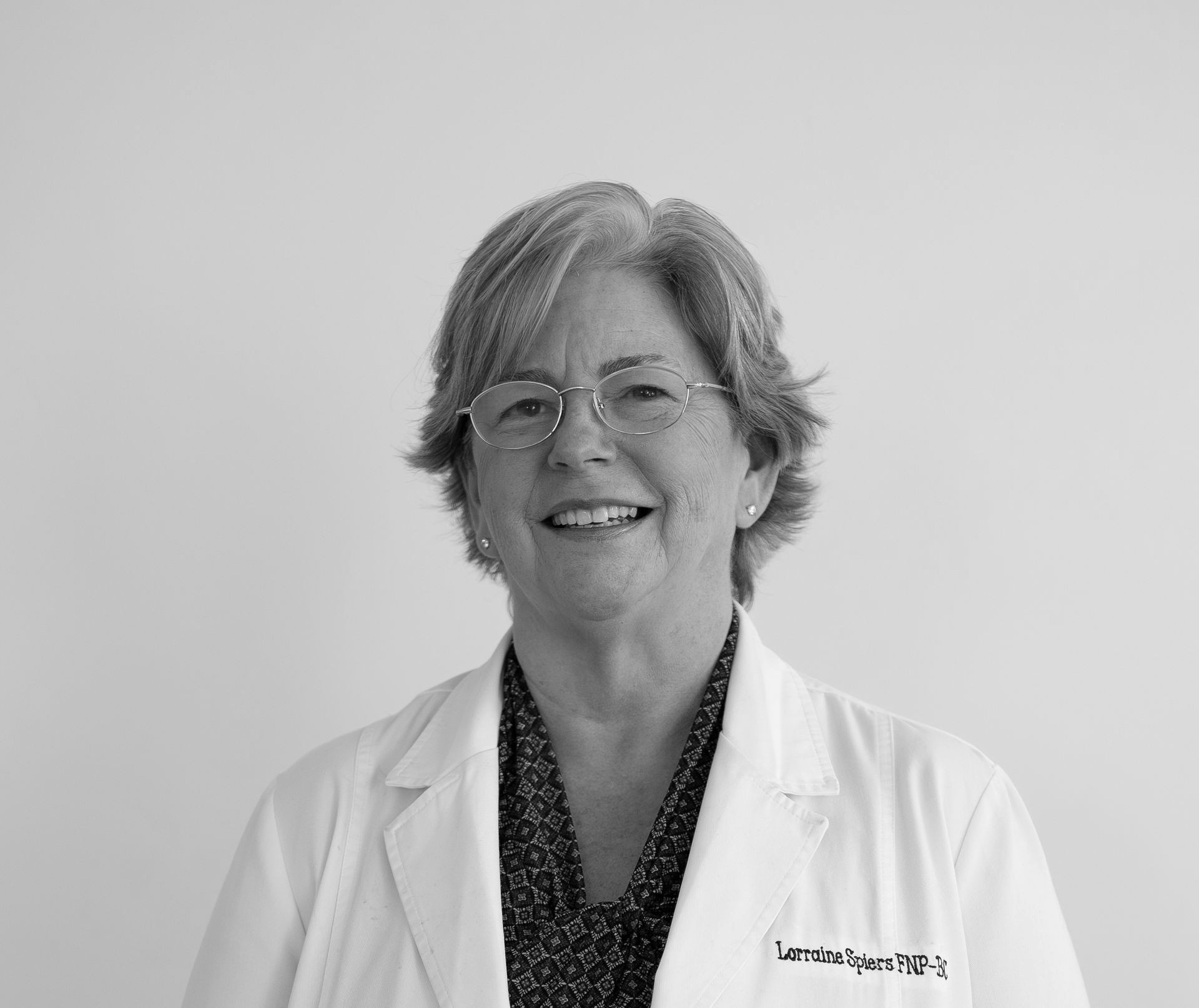 A woman wearing glasses and a black shirt is smiling in a black and white photo.