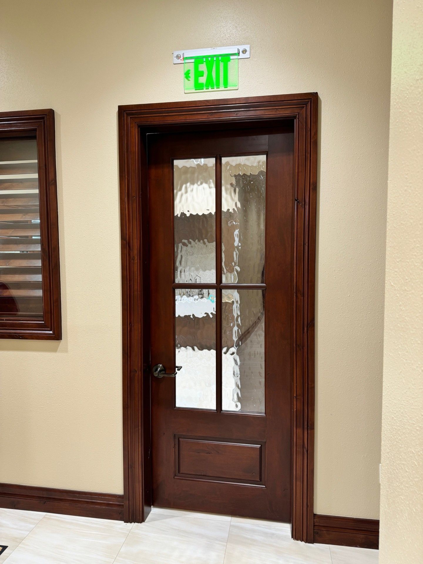 Wooden door with frosted glass panes beneath a green exit sign in a hallway