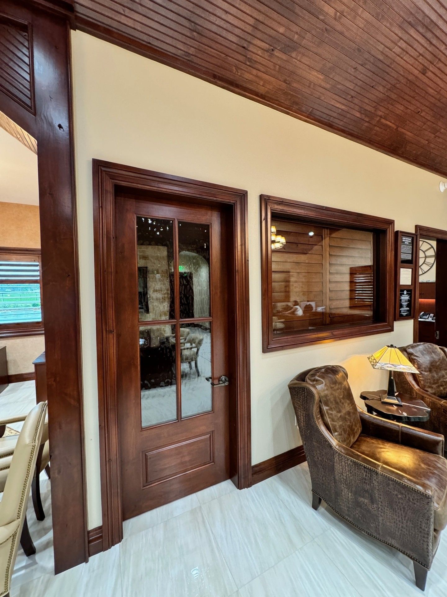 Wood-paneled hallway with a glass door, large window, and wicker chairs in a warm interior lounge