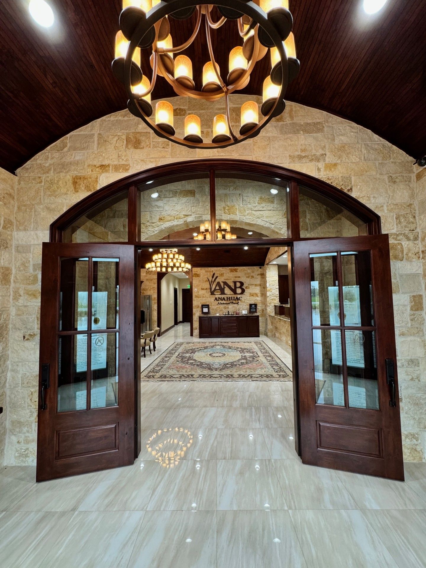 Grand arched wooden doorway opening to a marble-floored lobby with chandeliers and wall art.