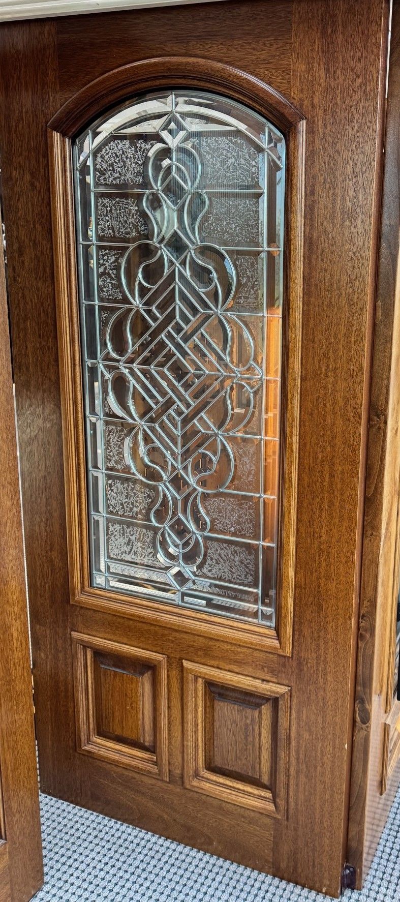 Wooden front door with an arched decorative glass panel and carved lower panels