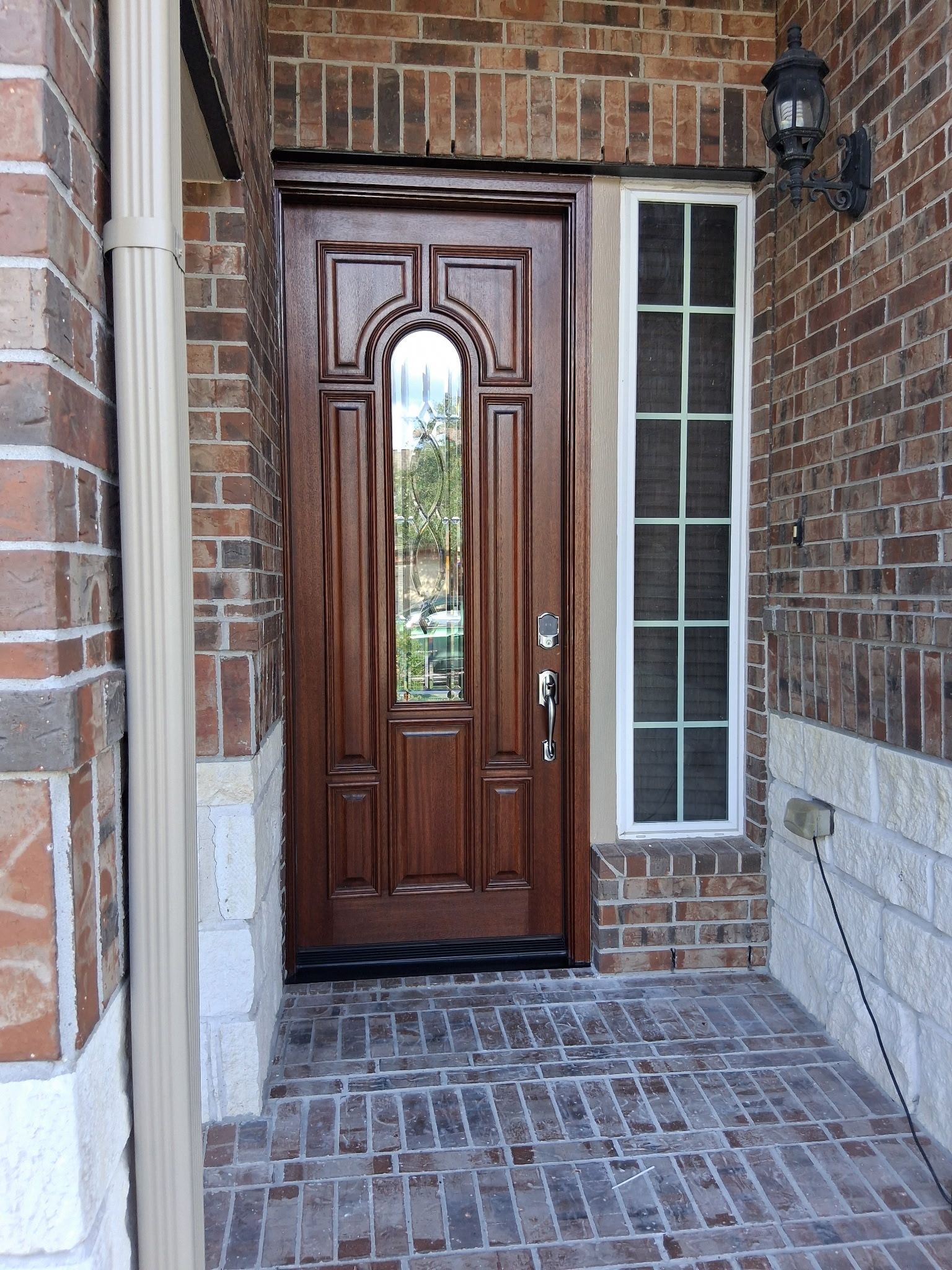 Front entrance with a wooden door, brick walls, and a tiled walkway under a covered porch