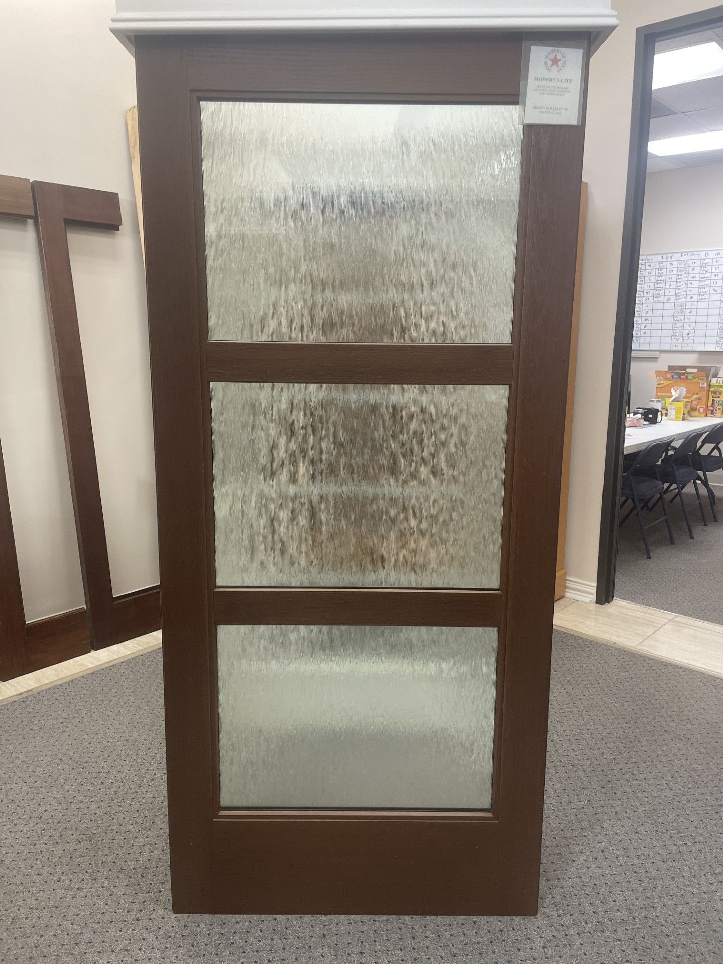 Wooden cabinet door with three frosted glass panels, standing in a showroom.