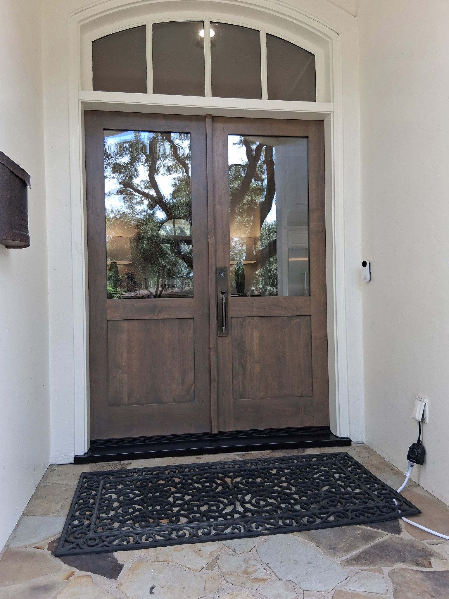 Wooden double front doors with glass panes, framed by a white archway and a patterned doormat.