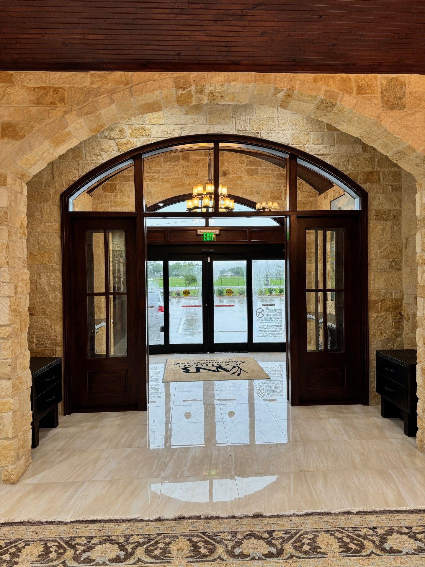 Stone entryway with arched wooden doors, glass double doors, and polished floor reflection