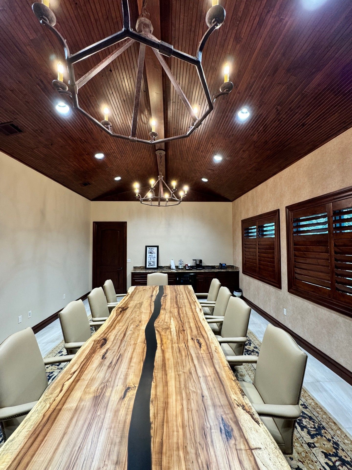 Modern conference room with a long wooden table, beige chairs, wood-paneled ceiling, and wall shutters