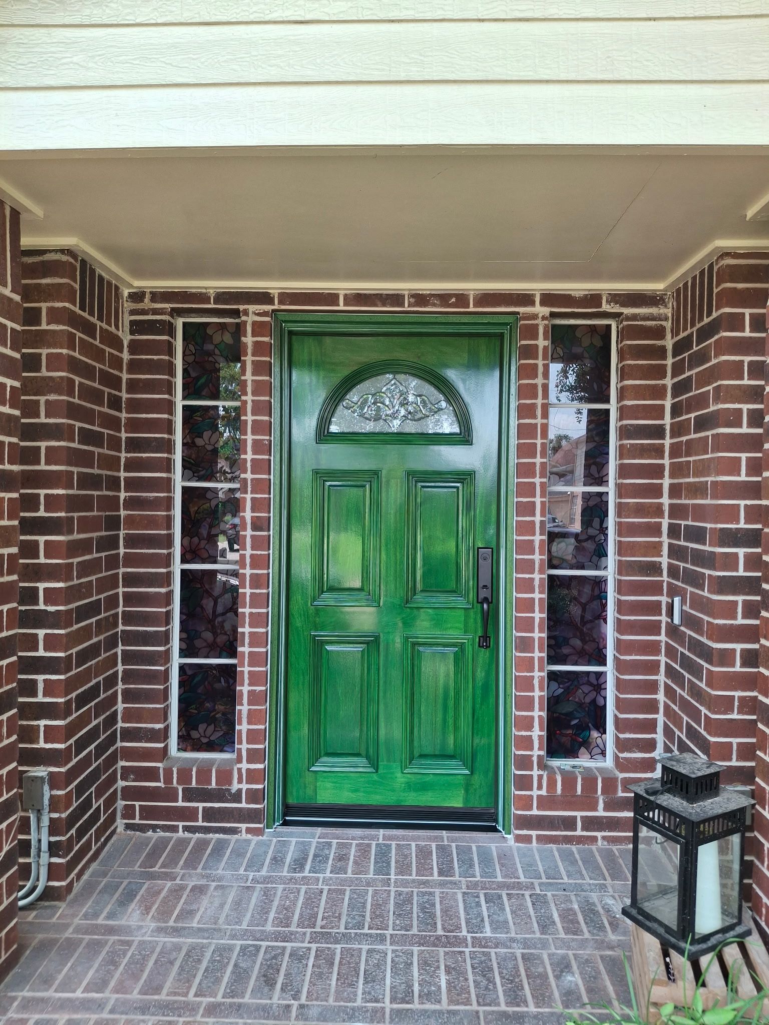 Front porch with a green front door, brick walls, sidelights, and a lantern by the entrance.