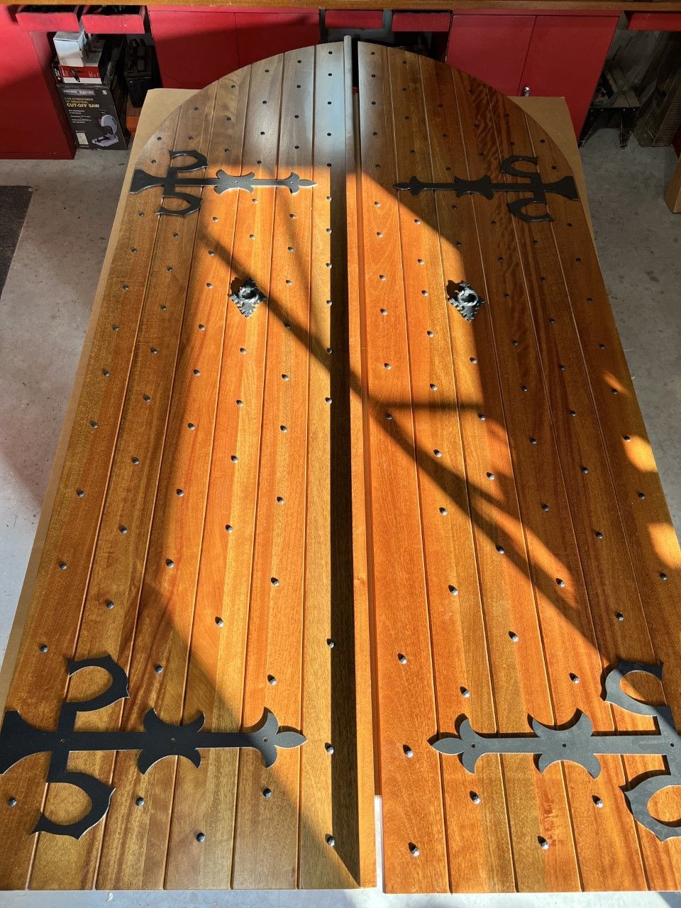 Wooden double doors with black iron hinges and a sunlit diagonal shadow