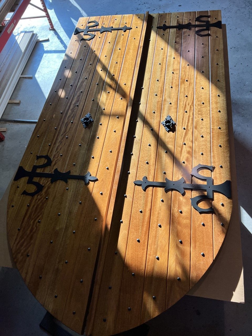 Wooden rustic barn door with black iron hinges, lit by sunlight and shadow