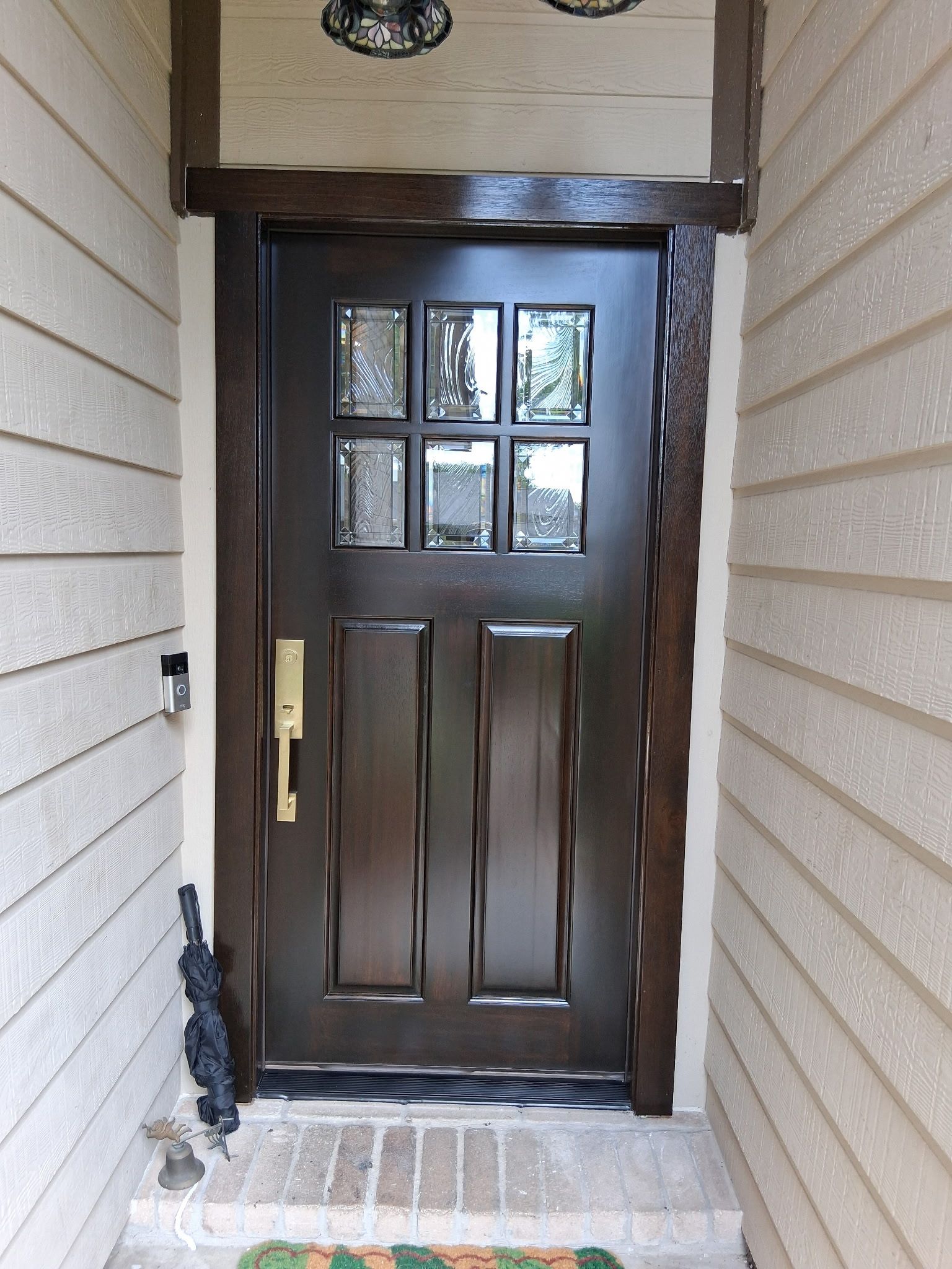 Dark brown front door with small window panes in a beige exterior entryway