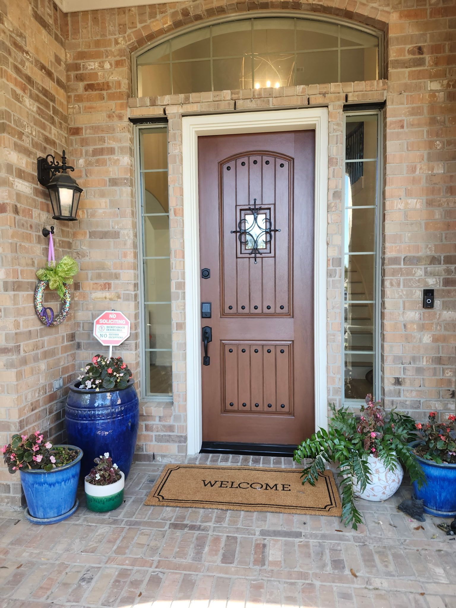 Front door of a brick house with potted plants and a brown welcome mat