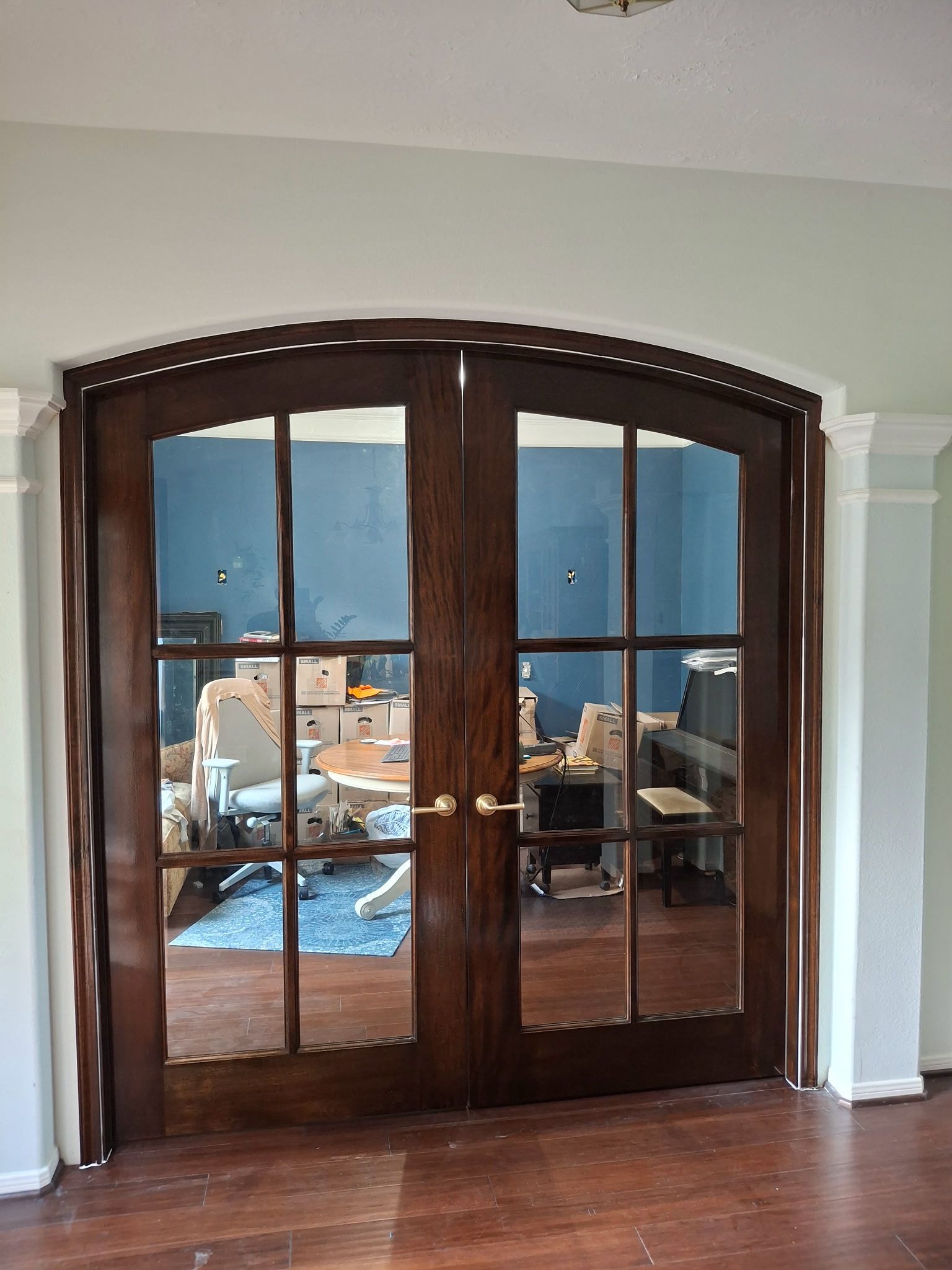 Double wooden French doors with arched transom opening into a furnished room with blue walls.