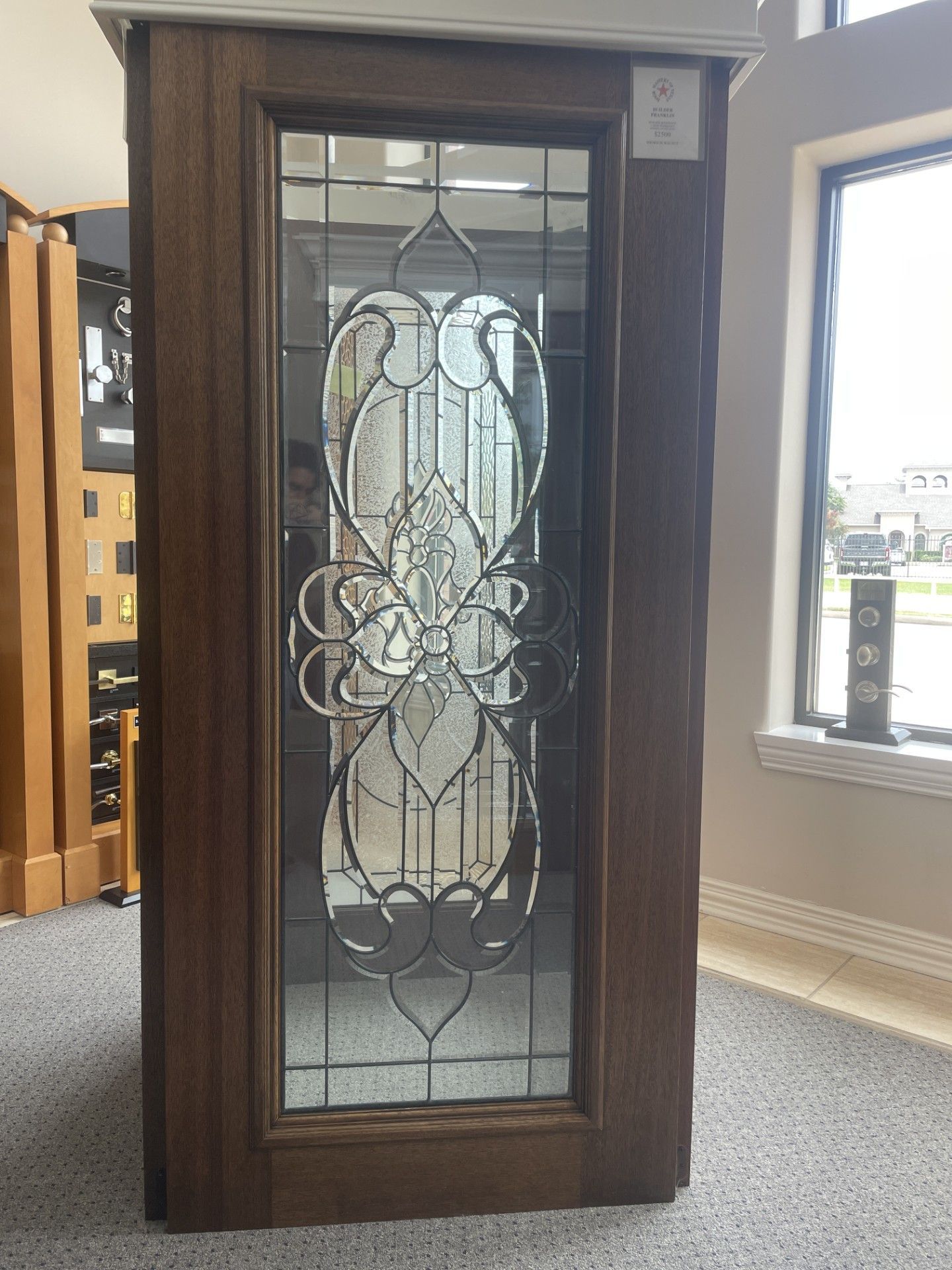 Tall wooden cabinet with a decorative glass front in a showroom, next to windows.
