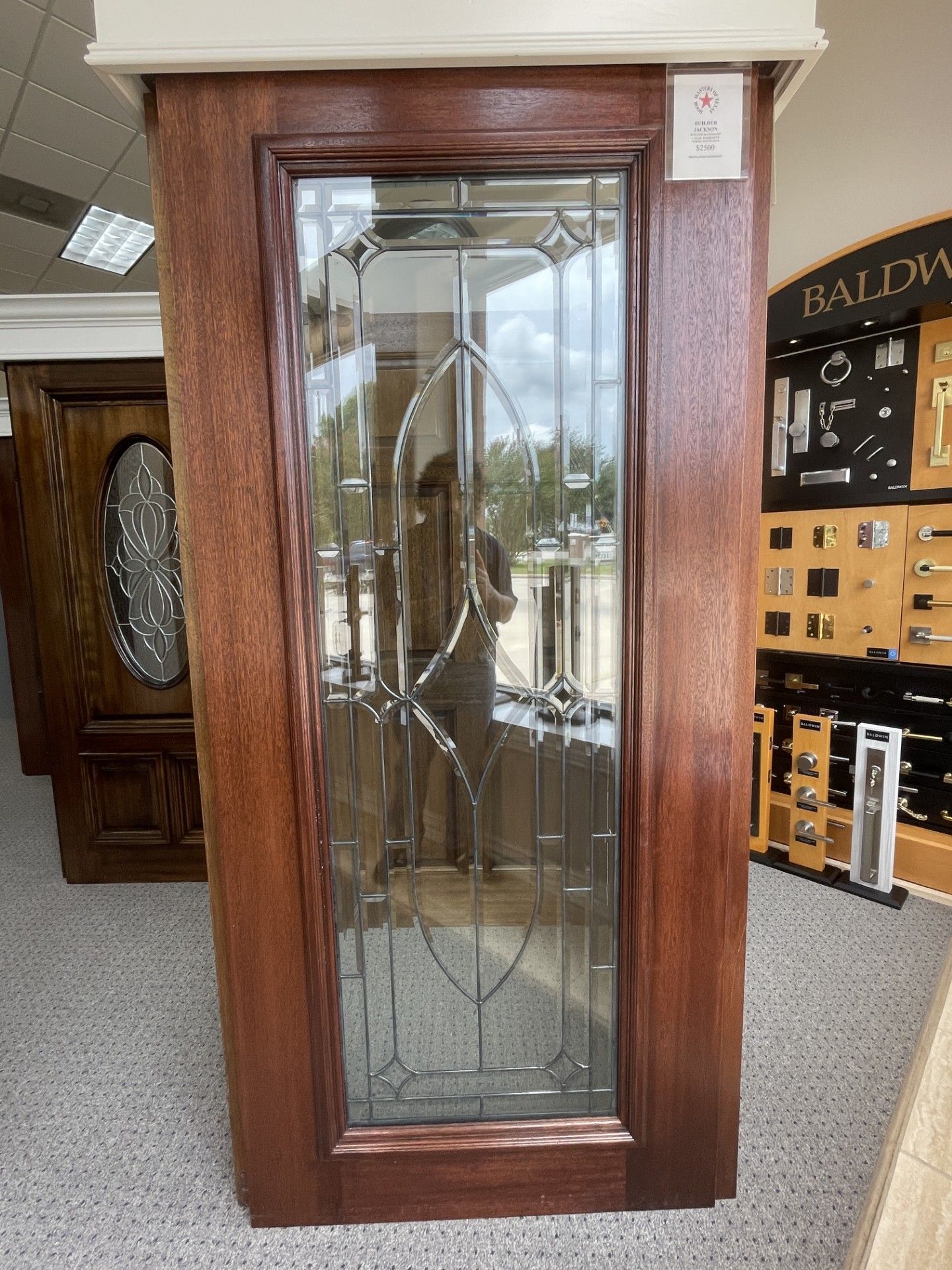 Tall wooden-framed glass display cabinet with decorative leaded glass panels in a showroom.