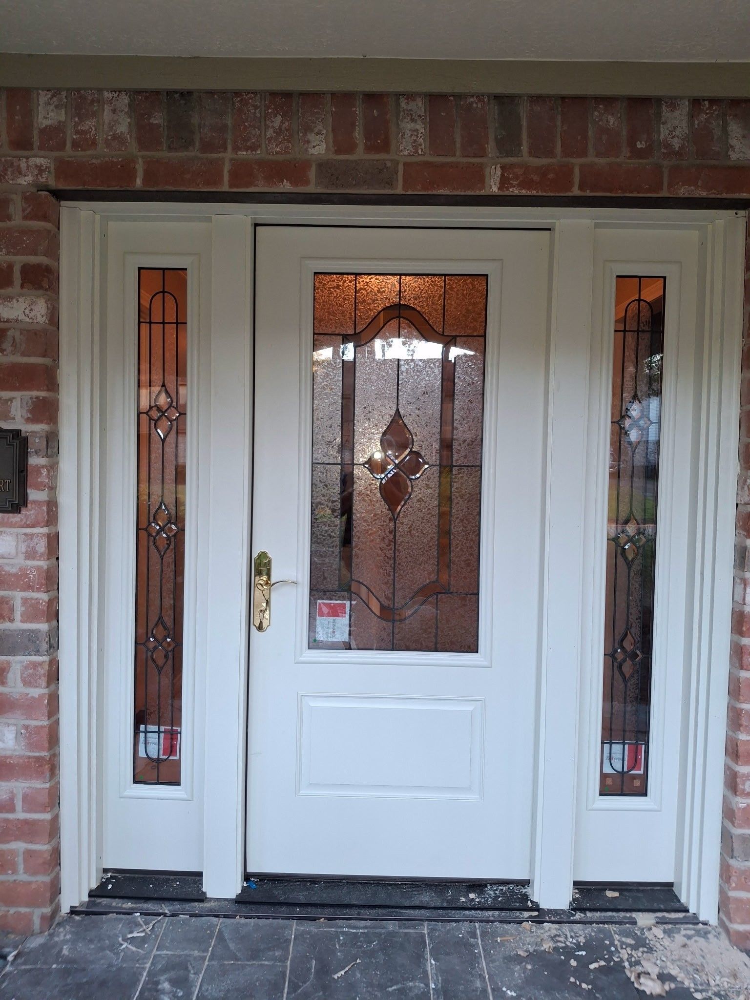 White front door with decorative glass sidelights and a brick exterior surround