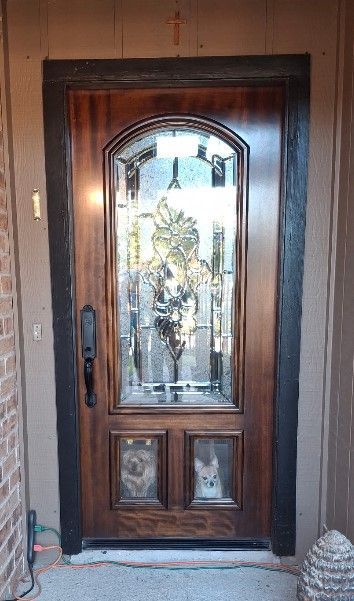 Wooden front door with decorative glass panels and black handles, set in a brown exterior wall.