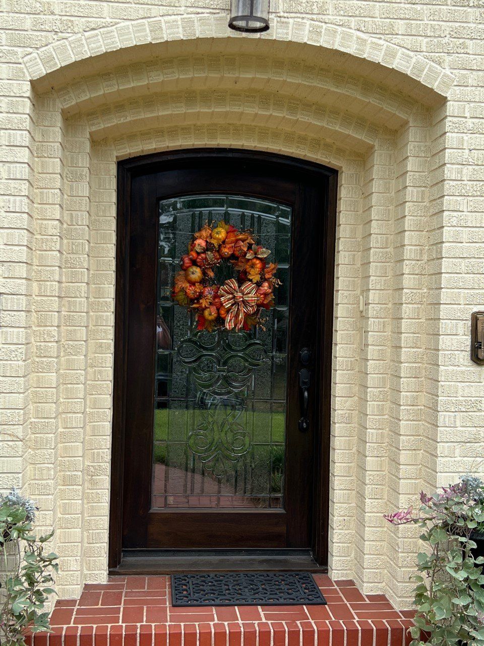 Front door with glass inset and autumn wreath set in a cream brick archway above red steps