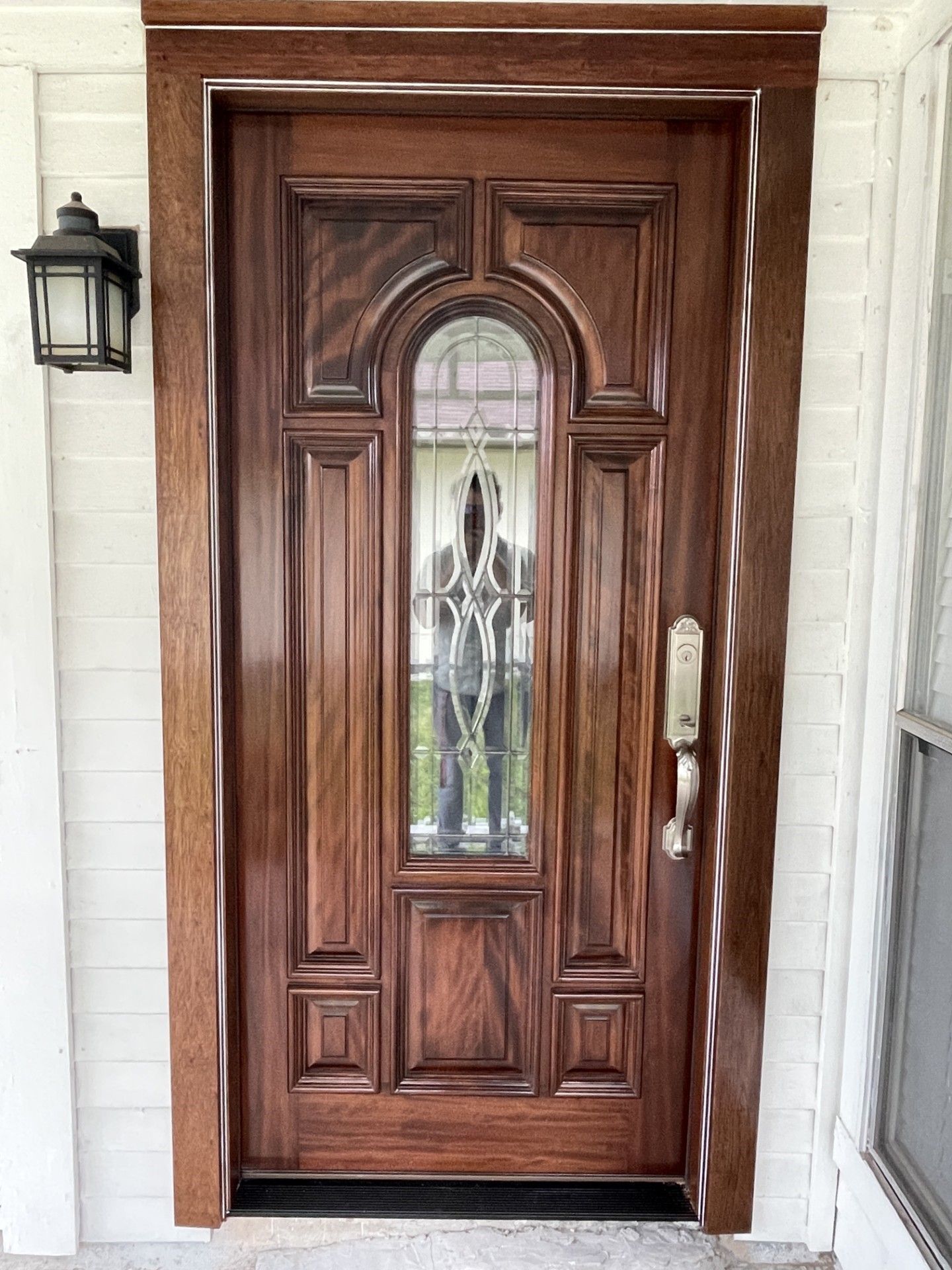 Wooden front door with decorative glass panel and silver handle beside a wall lantern
