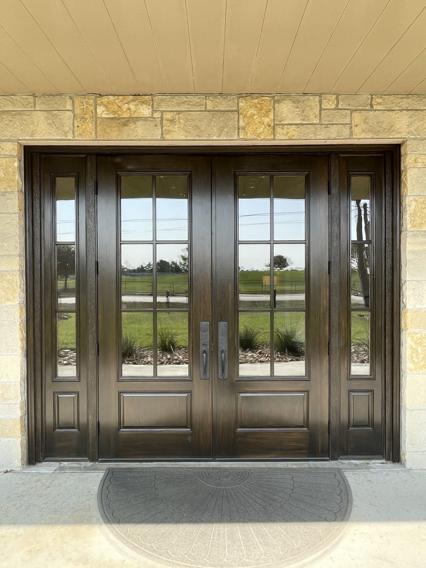 Double glass entrance doors with dark wood frames under a stone archway