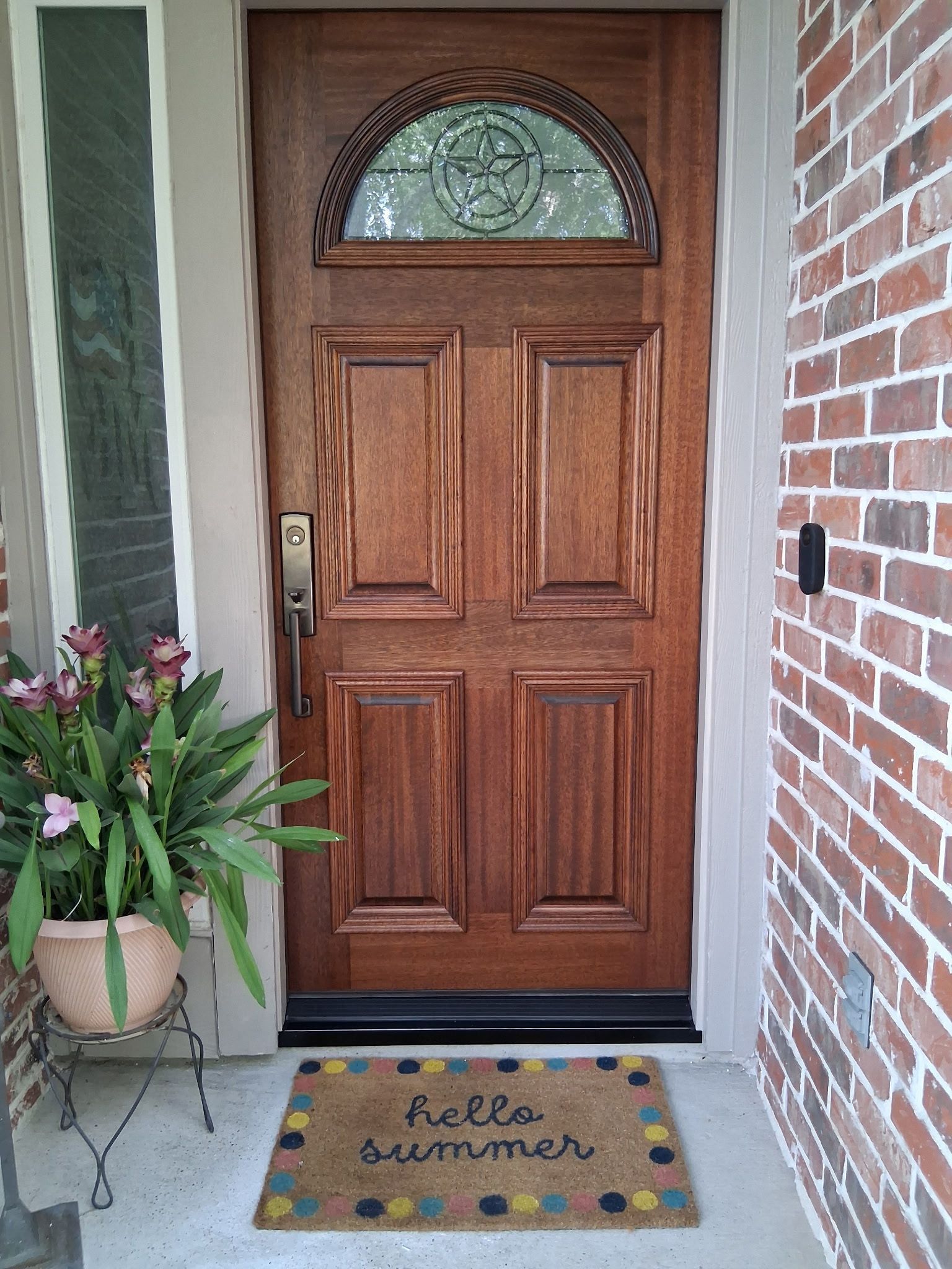 Front porch with wooden door, potted flowers, and doormat reading “Hello Sunshine.”