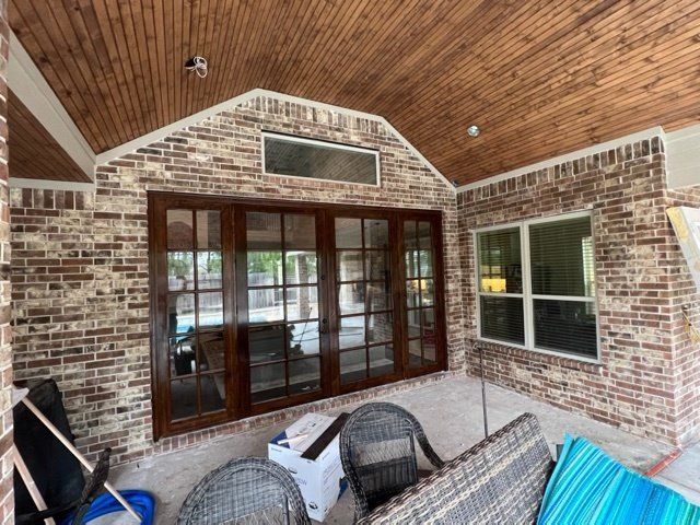 Covered brick patio with vaulted wood ceiling, French doors, window, and wicker furniture.