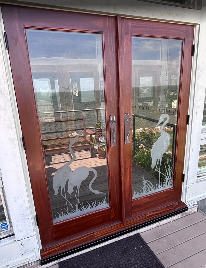 Wooden patio doors with frosted white dog silhouettes and a deck mat outside