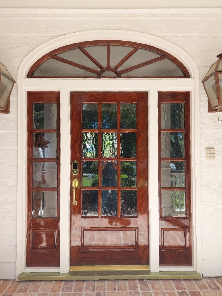 Front door with arched transom, wood-and-glass panels, and sidelights on a cream facade.