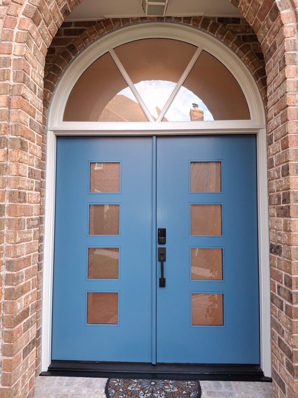 Blue double front doors with small square windows under a brick archway