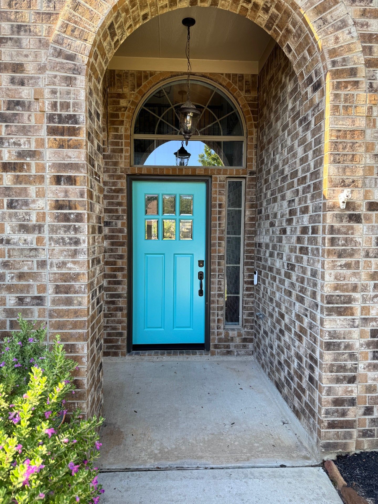 Bright turquoise front door set in a brick archway with a small flower bed nearby