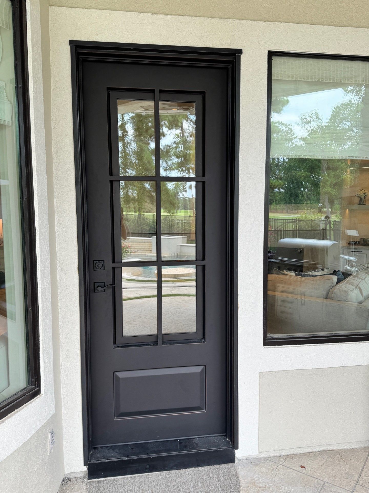 Black front door with glass panes beside windows on a porch.