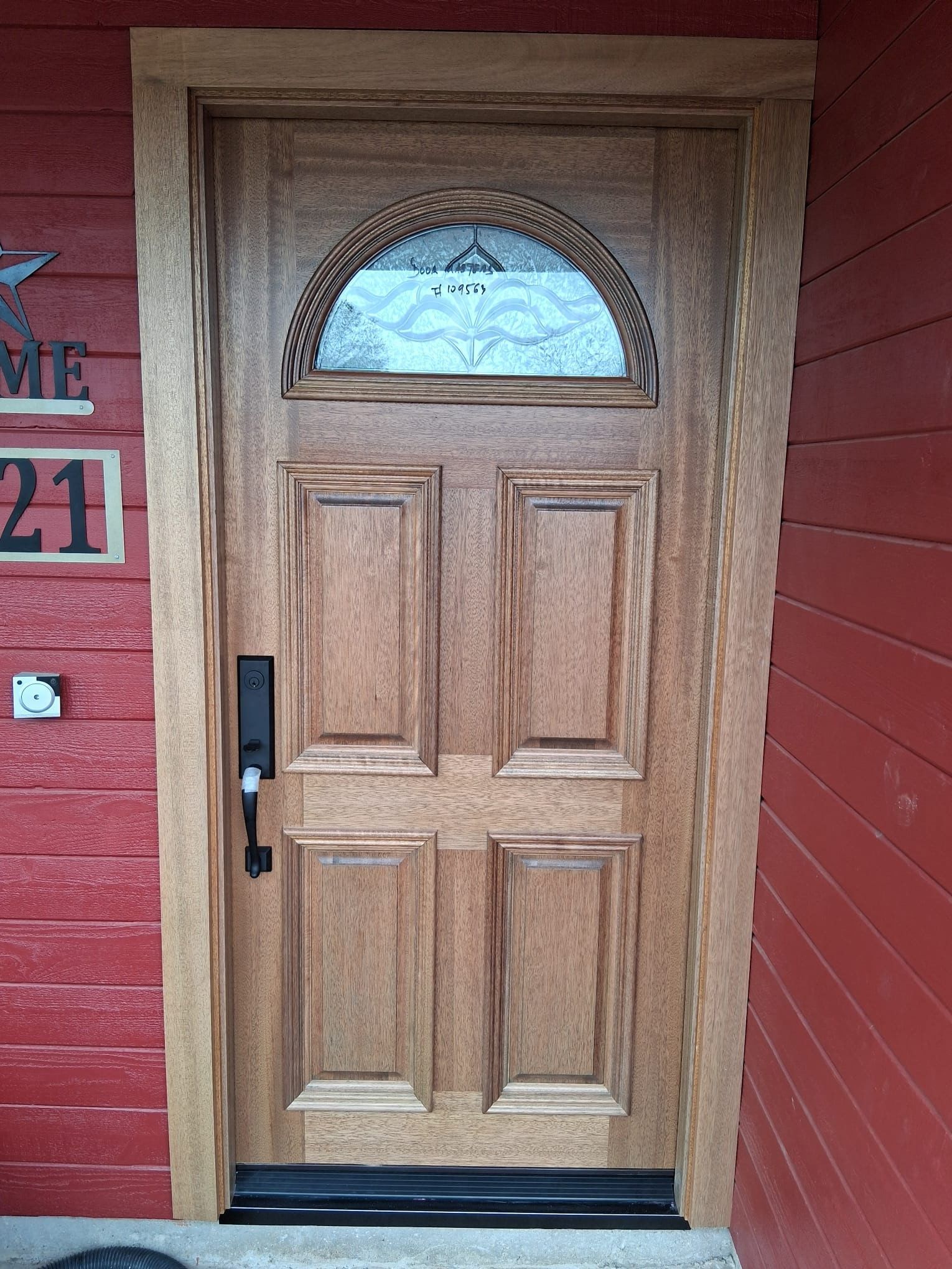 Wooden front door with a half-circle glass window in a red house entryway.