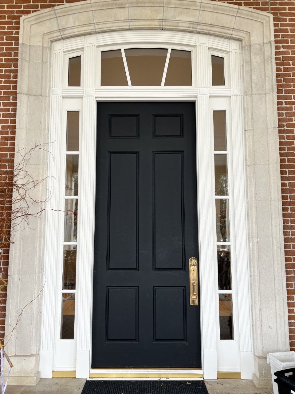 Black front door with white trim and sidelights set in a brick entryway