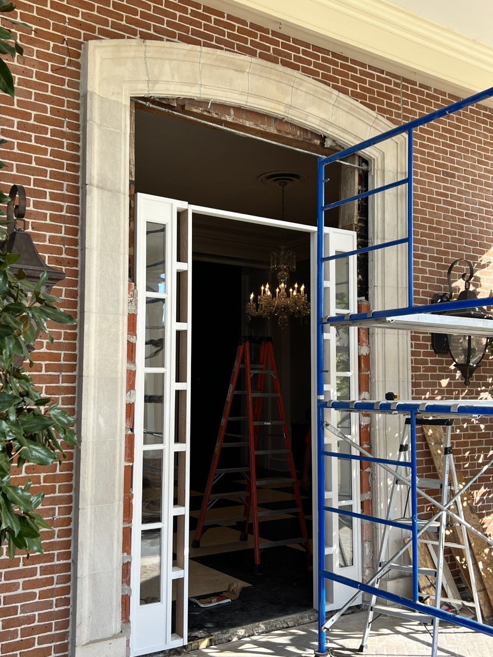 Open brick doorway with white French doors, a red ladder inside, and blue scaffolding outside.