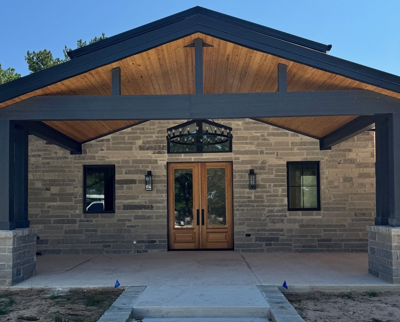 Front entrance of a stone building with dark trim, wooden double doors, and covered porch