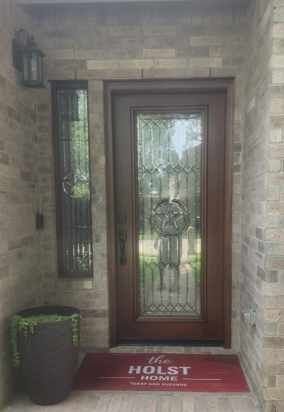 Front entry with a wooden door, side window, brick walls, and a red HOLST welcome mat.