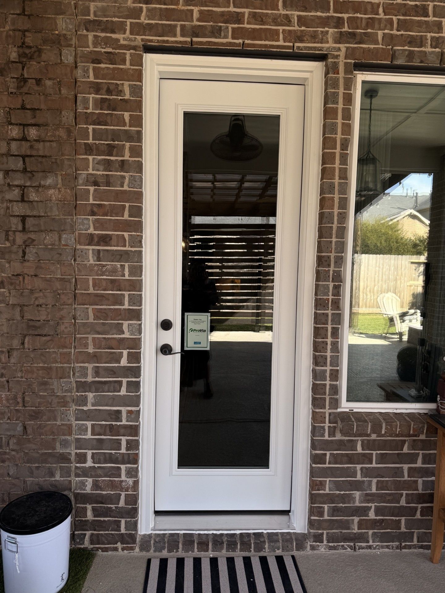 White exterior door with glass panel set in a brick wall beside a window.
