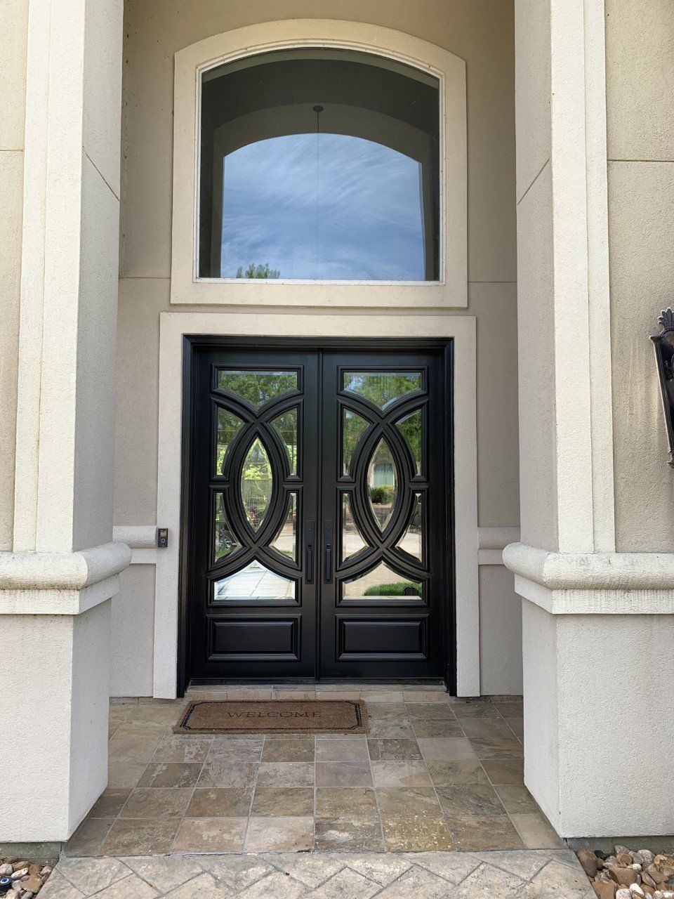 Front entry with black double doors, arched window, and beige stone facade.