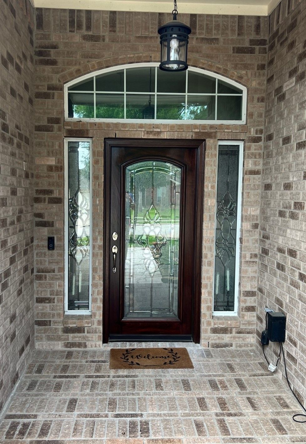 Brick front porch with a dark wood front door, sidelights, and arched transom window