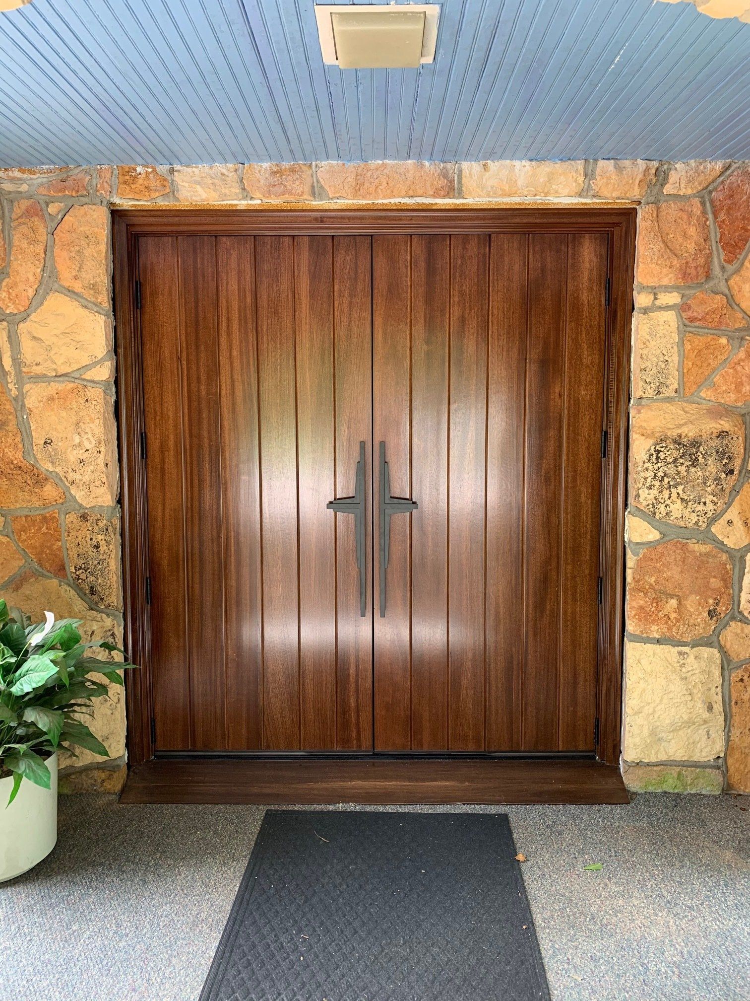 Wooden double doors set in a stone wall, with a mat on the ground outside.