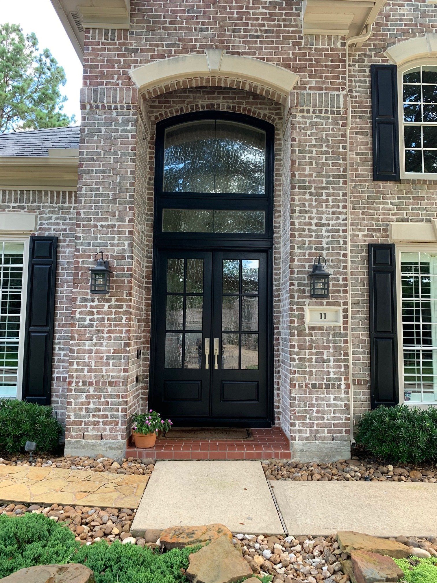 Brick house entry with arched black front door, flanked by windows and a front walkway.