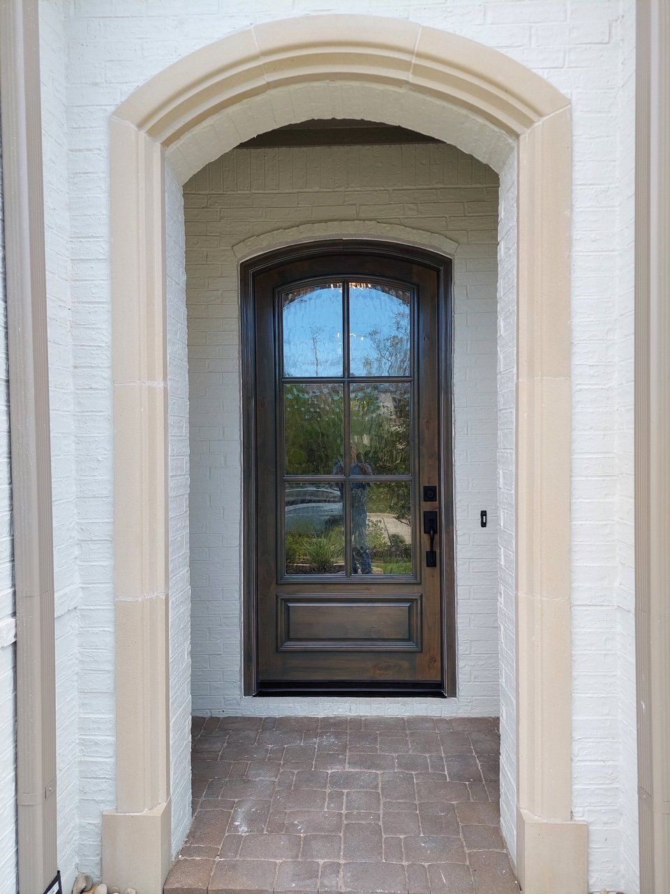 Arched entryway with a dark wood front door and tiled porch, framed by beige stucco walls.