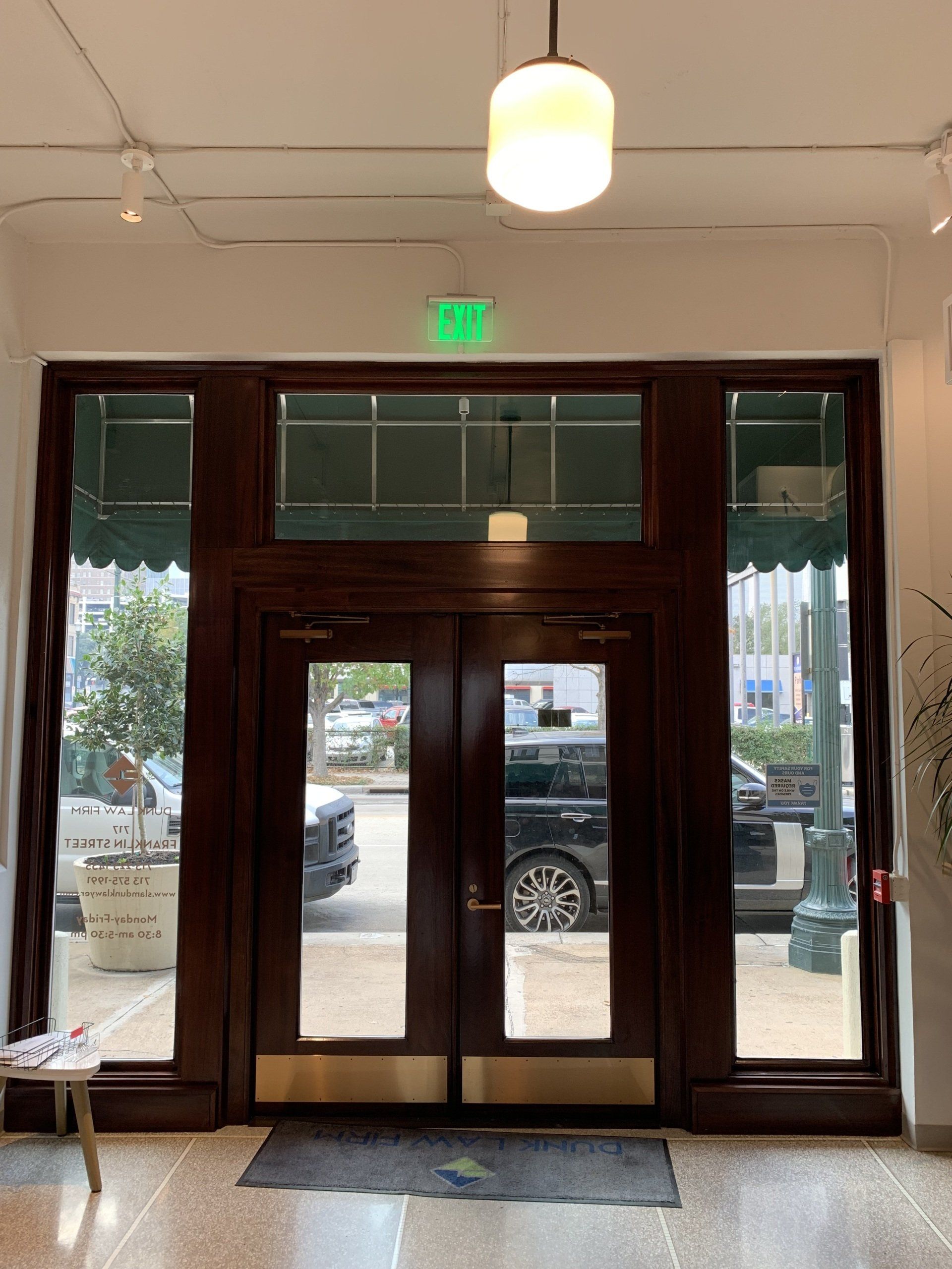 Glass-front entrance with dark wood doors, sidelights, and a hanging light inside a lobby.