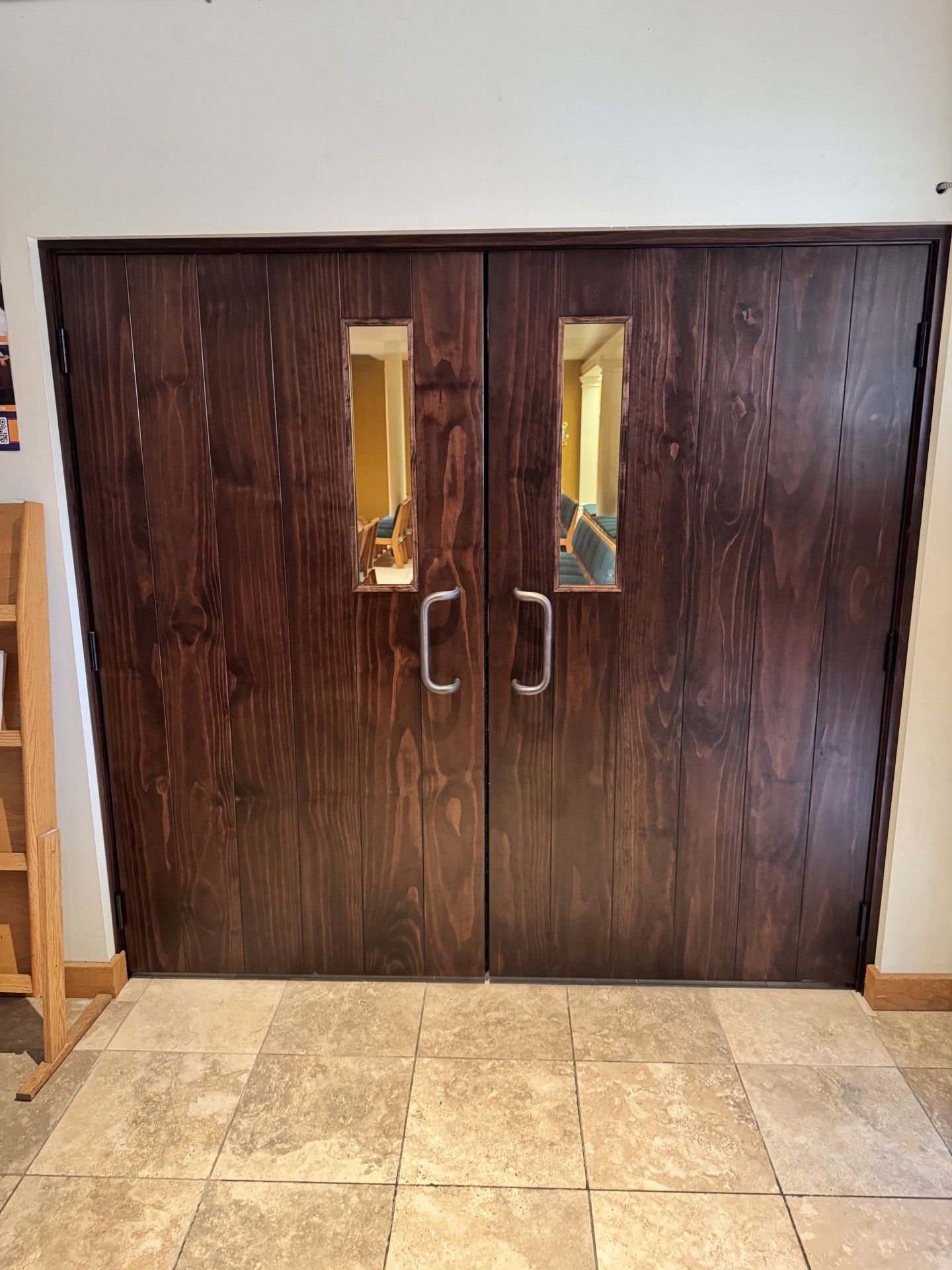 Double wooden doors with narrow windows in a tiled hallway