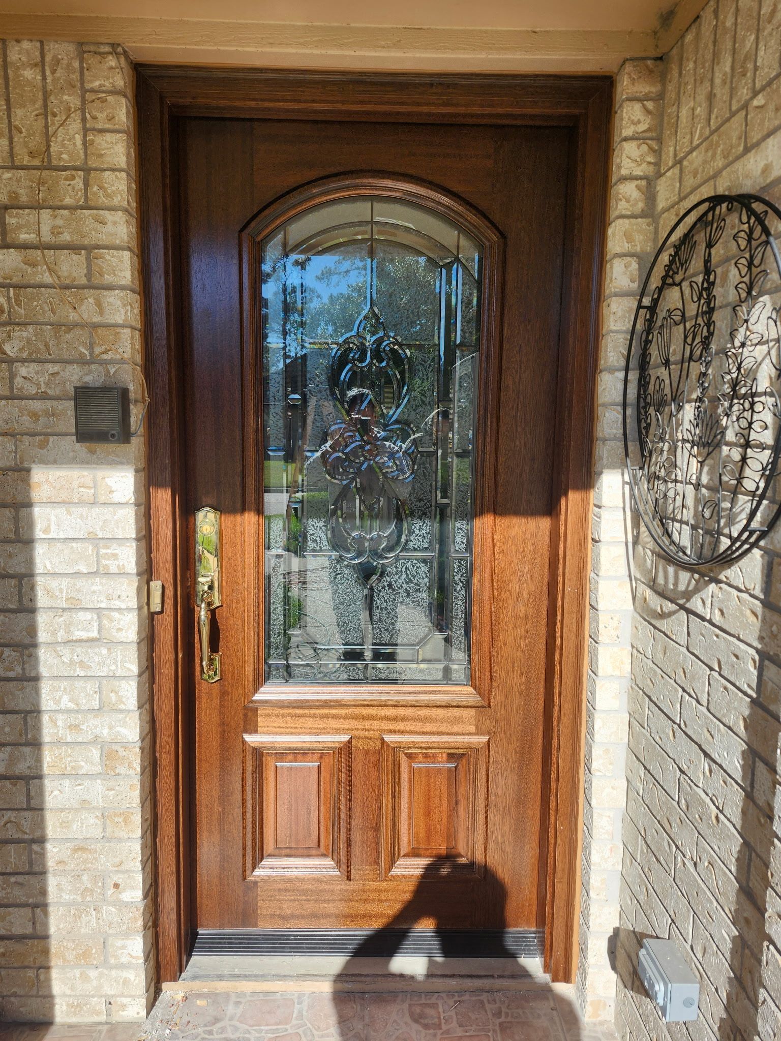 Wooden front door with arched glass panel, set in a stone entryway with a decorative wall plaque.