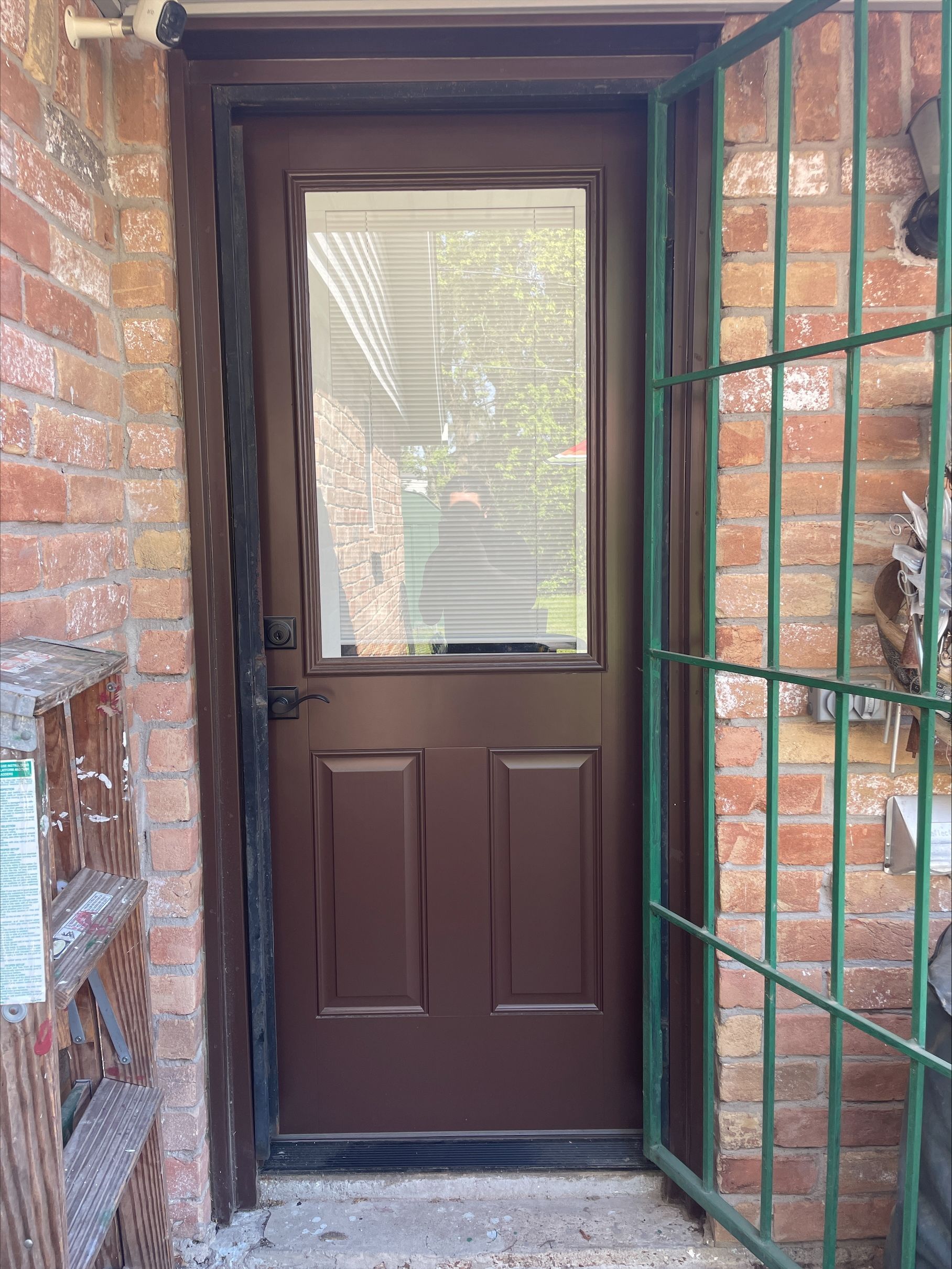 Brown door with glass panel in a brick entryway, partially open to a small porch with metal trellis.