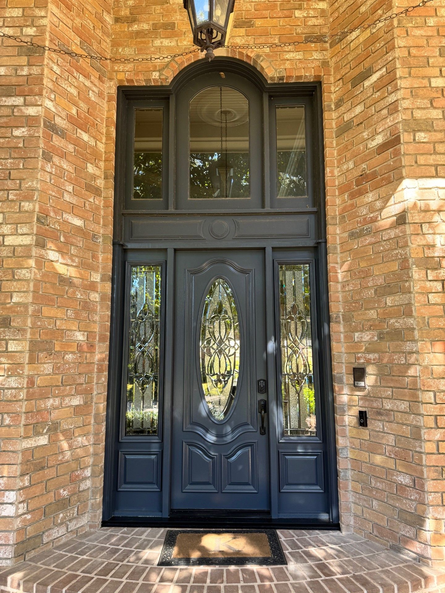 Black double front door with decorative glass in a brick entryway