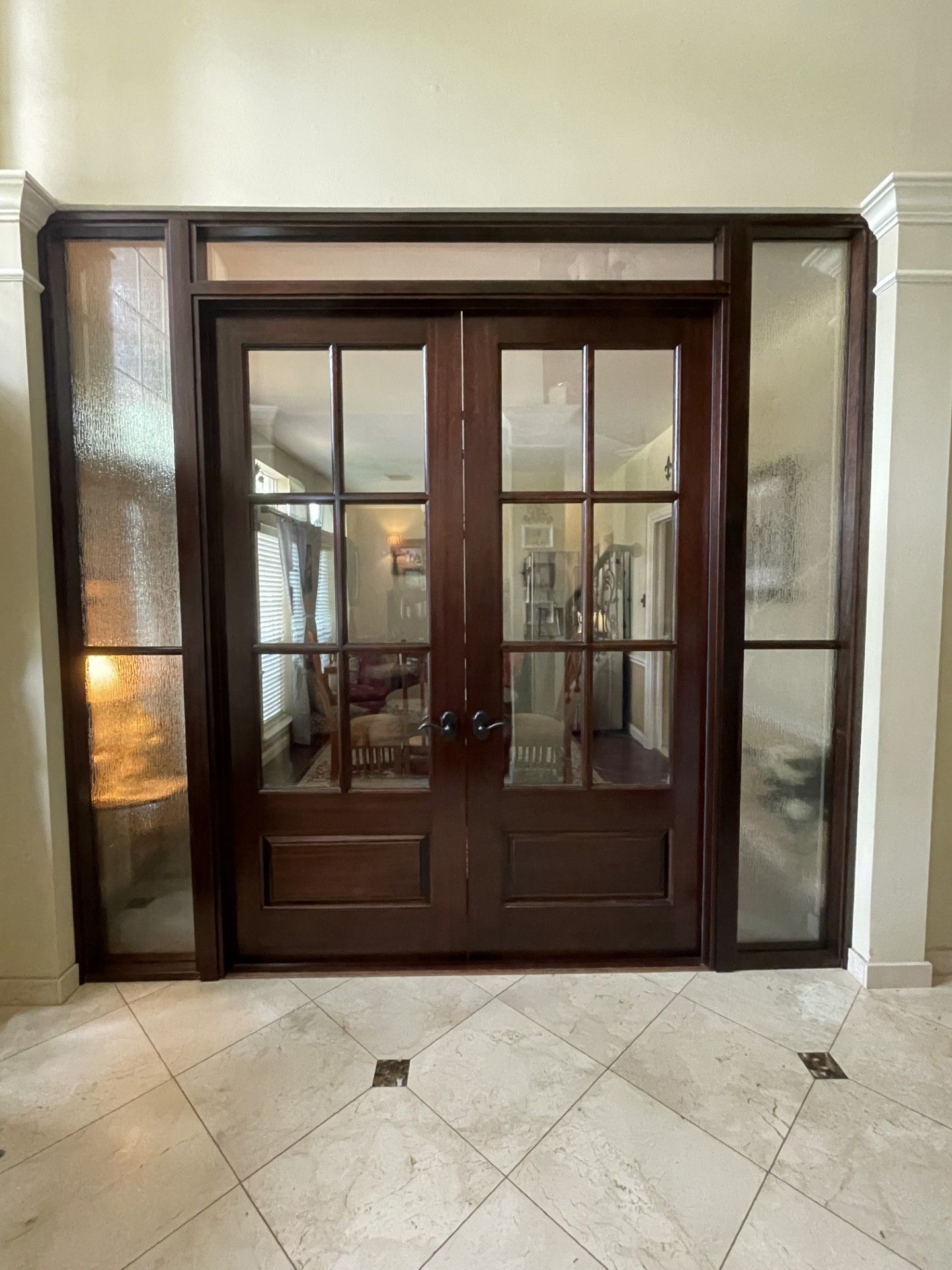 Wooden double doors with glass panes in a marble foyer, framed by frosted side panels.