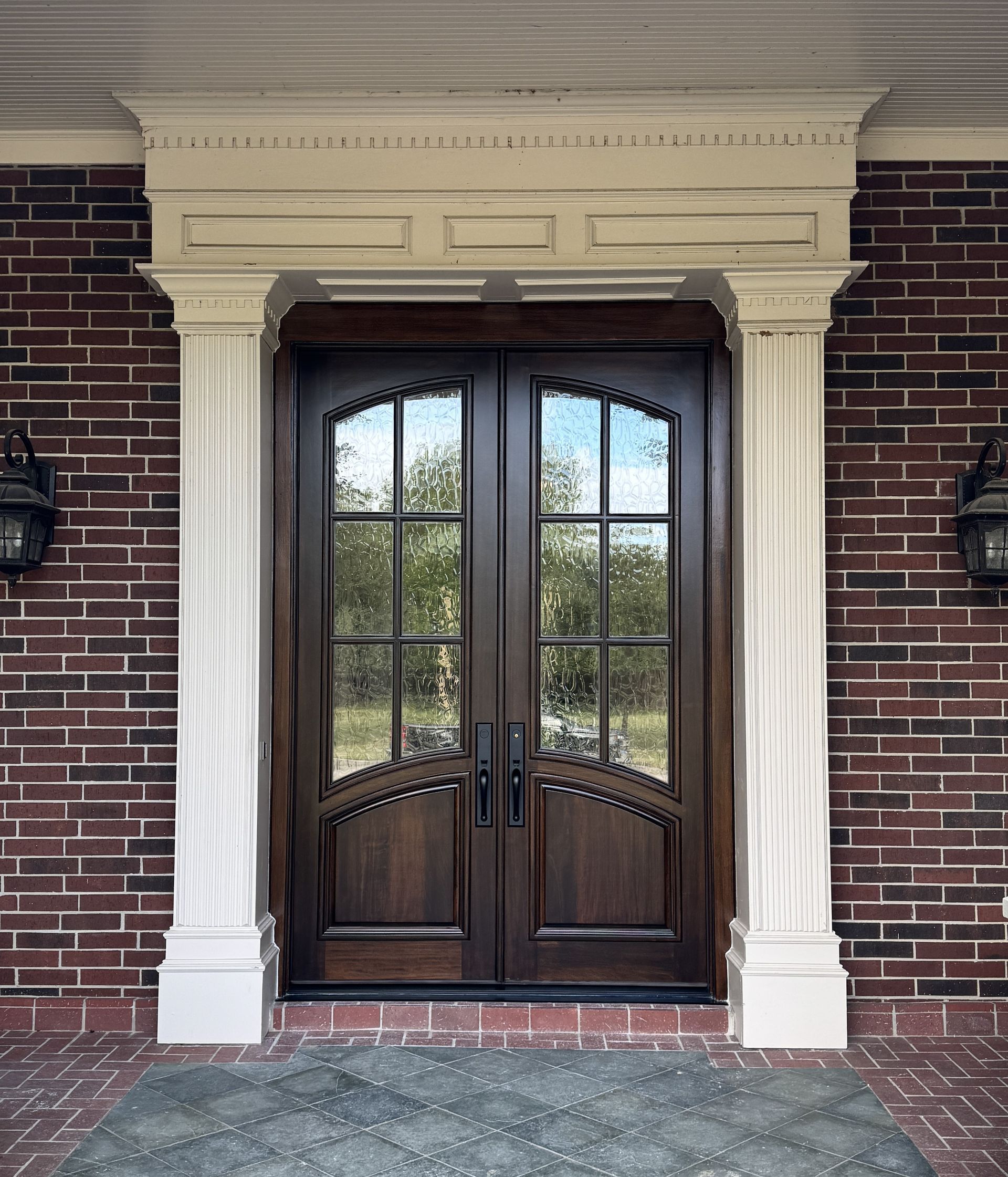 Double front door with arched glass panes and white columns set in a brick entryway